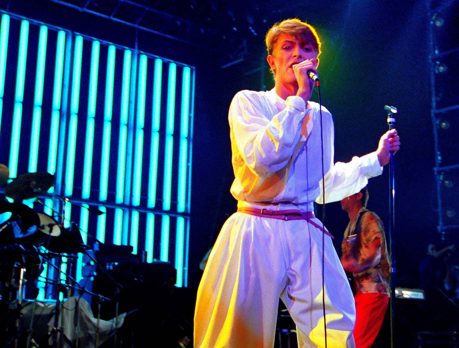 David Bowie singing into a microphone on a blue-lit stage in an archival publicity photograph supplied for Stage.
