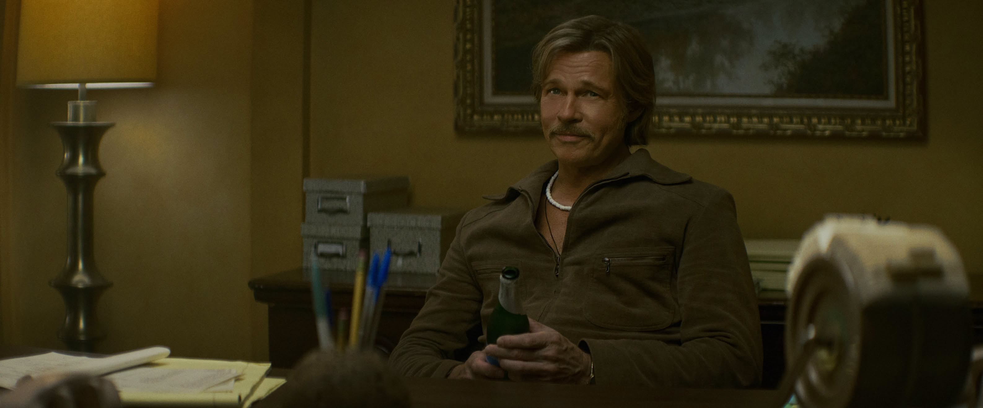 Brad Pitt as Cliff Booth seated in an office in The Further Mis-Adventures of Cliff Booth.