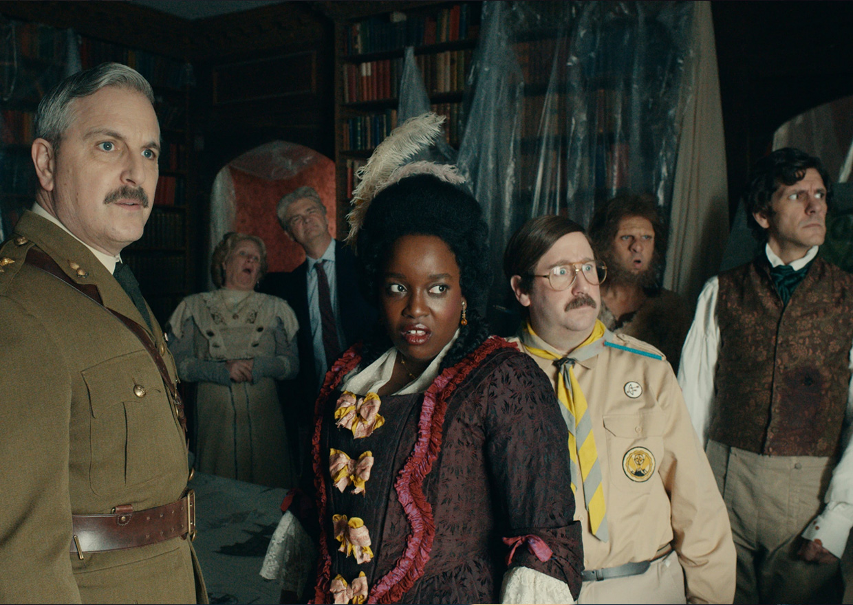 The Ghosts cast in period costume look across a room in Button House.