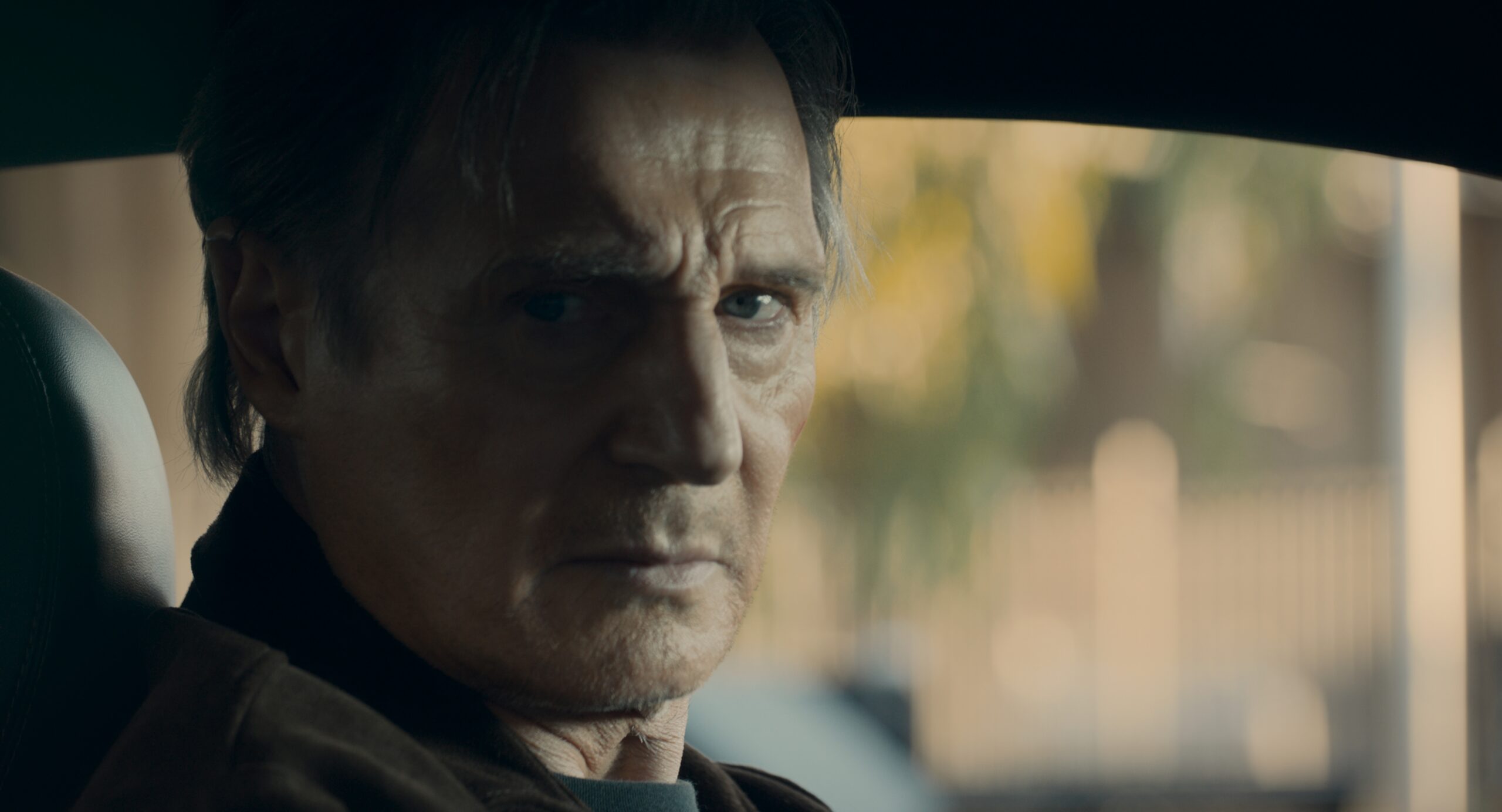 Liam Neeson as Ryan Flanagan looks across the front seat of a car in The Mongoose.