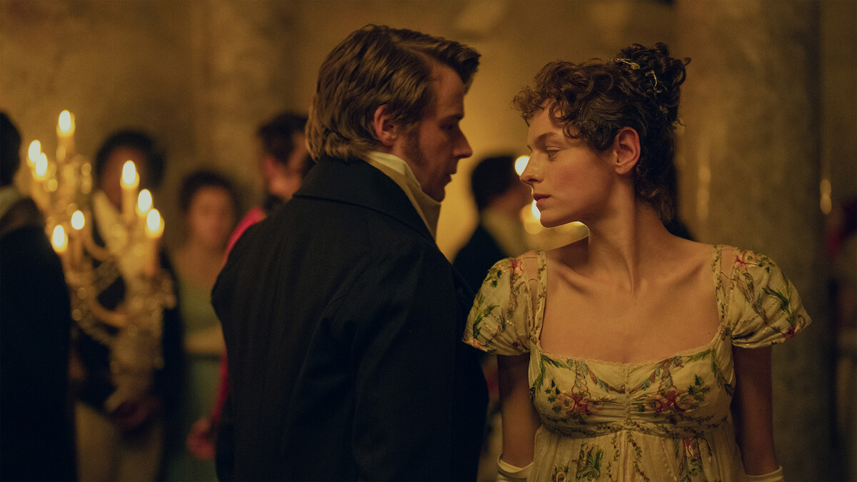 Jack Lowden as Mr Darcy and Emma Corrin as Elizabeth Bennet in a candlelit ballroom in Pride and Prejudice.