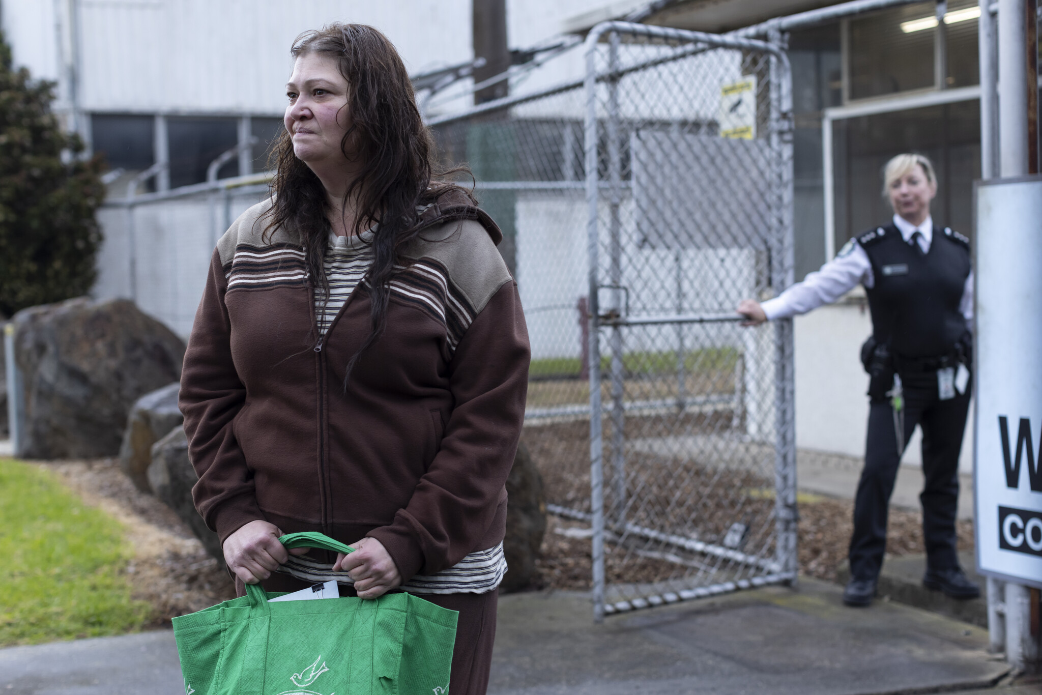Katrina Milosevic as Boomer outside the prison gate, holding a green bag, with Jacquie Brennan as Smiles behind her.